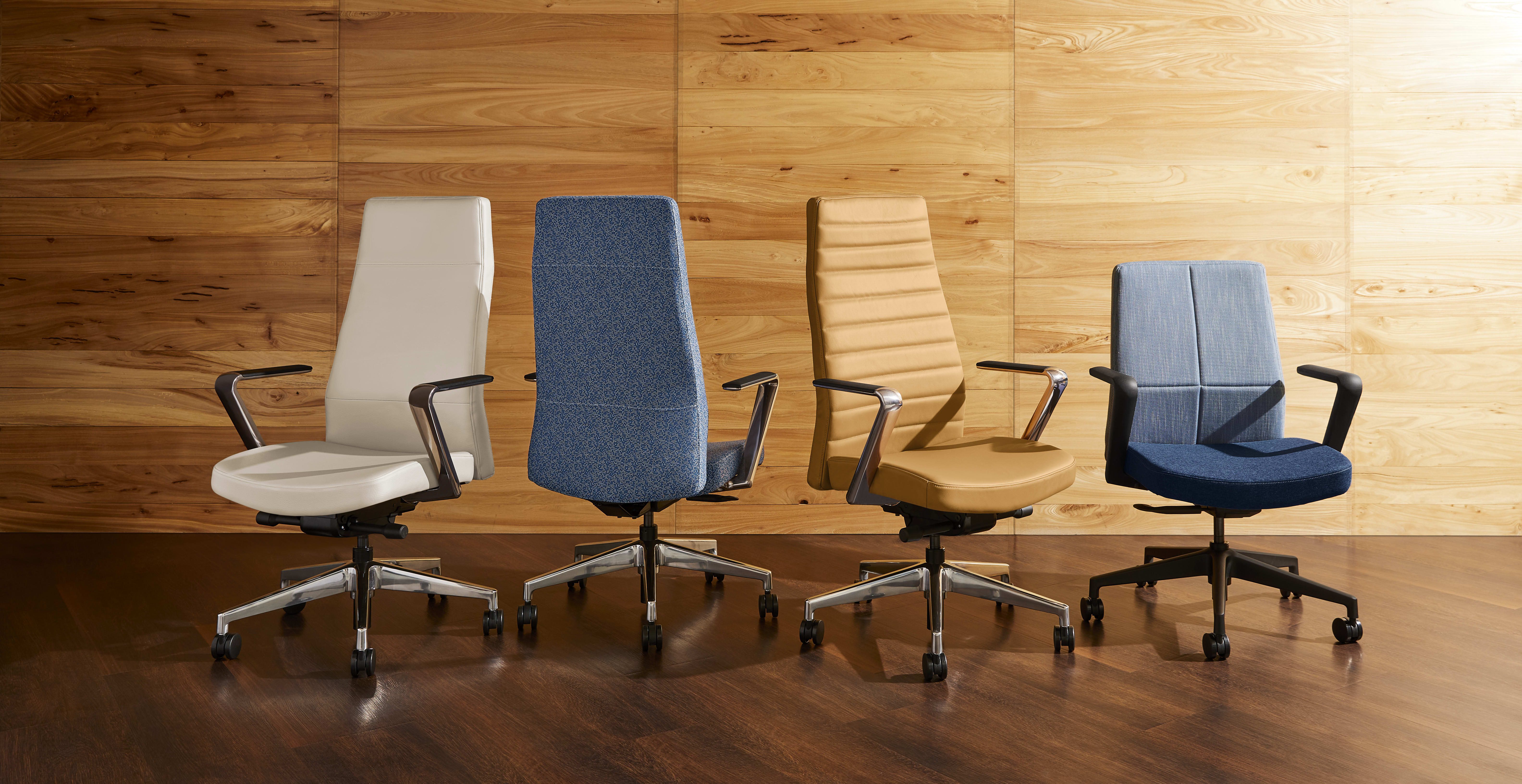 The image shows several office chairs of different designs and colors arranged in front of a wooden wall.