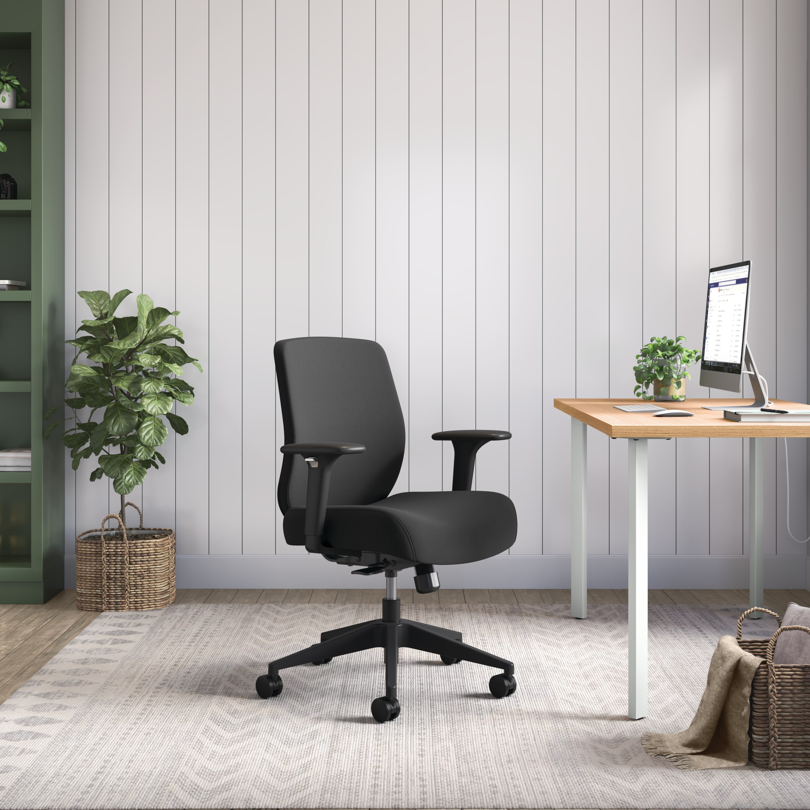 A modern, minimalist home office with a black ergonomic office chair, a wooden desk, and a potted plant in the background.