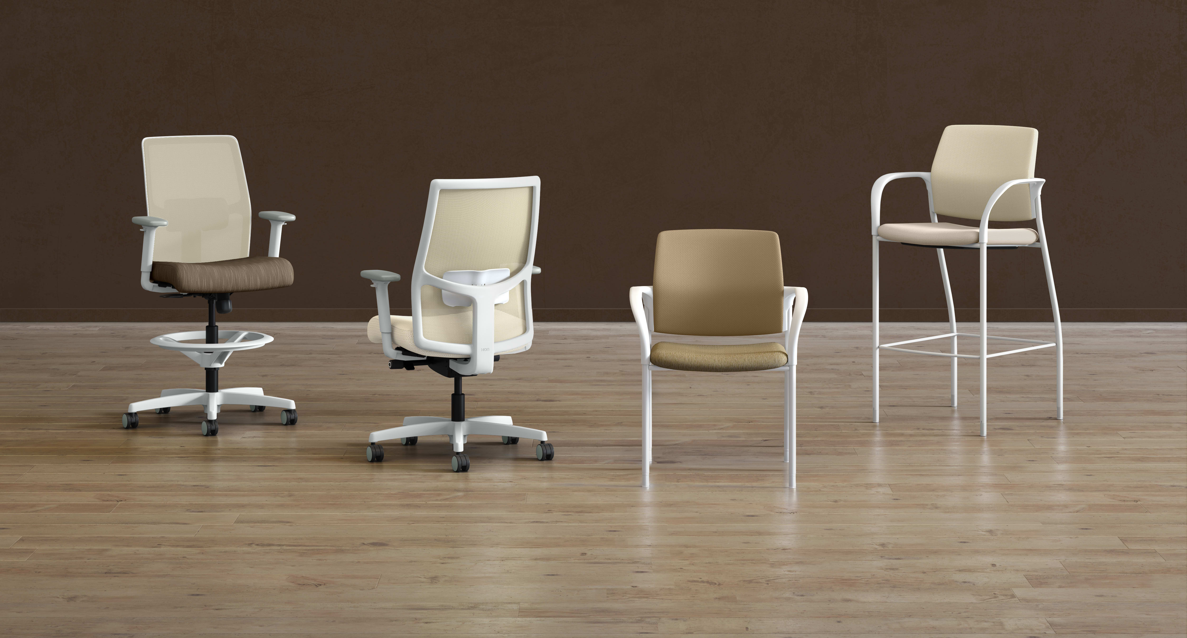 A collection of modern office chairs in various styles and colors, arranged on a wooden floor against a plain brown background.
