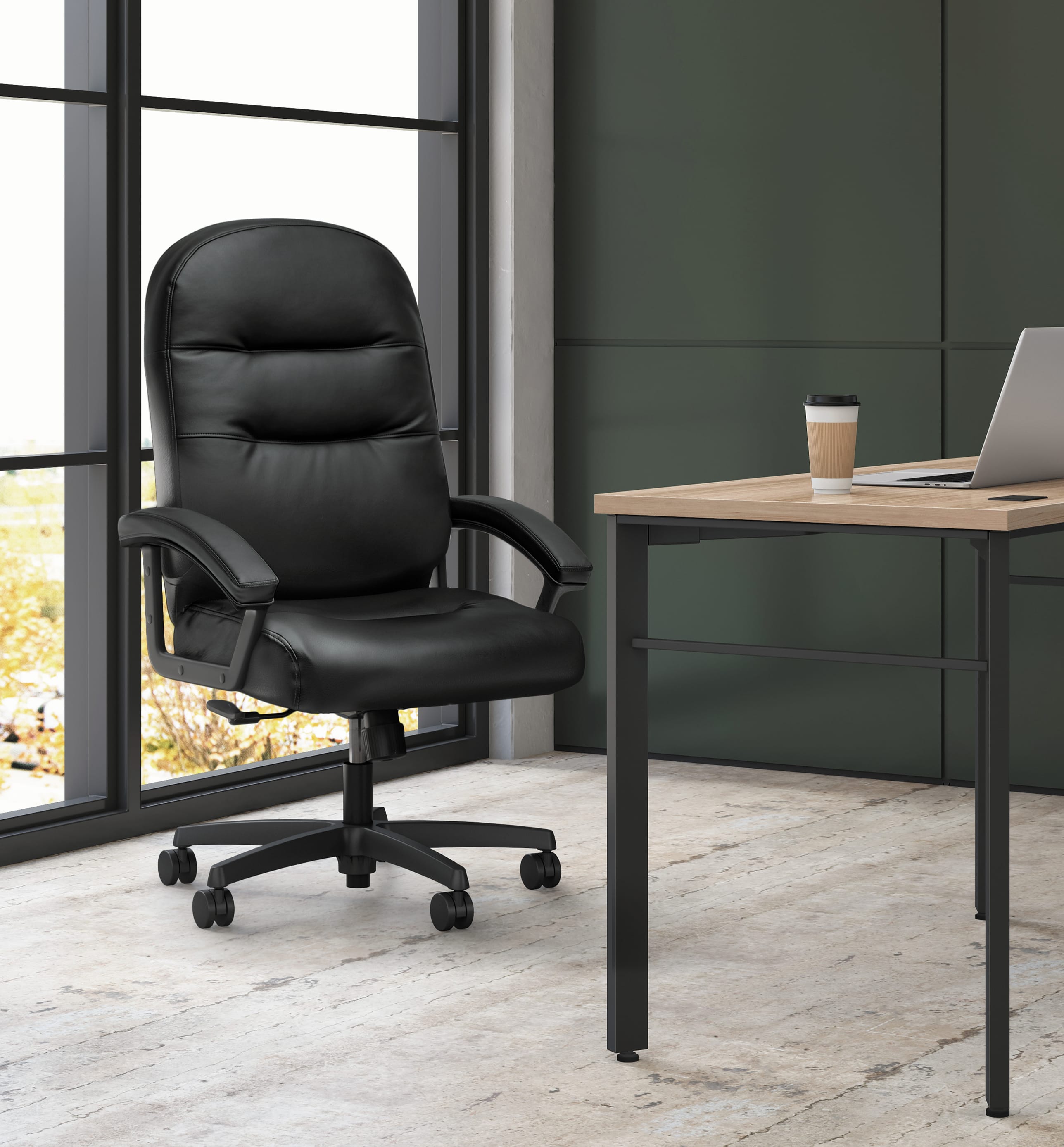 A black leather office chair sits in front of a large window, with a wooden desk and laptop visible in the background.