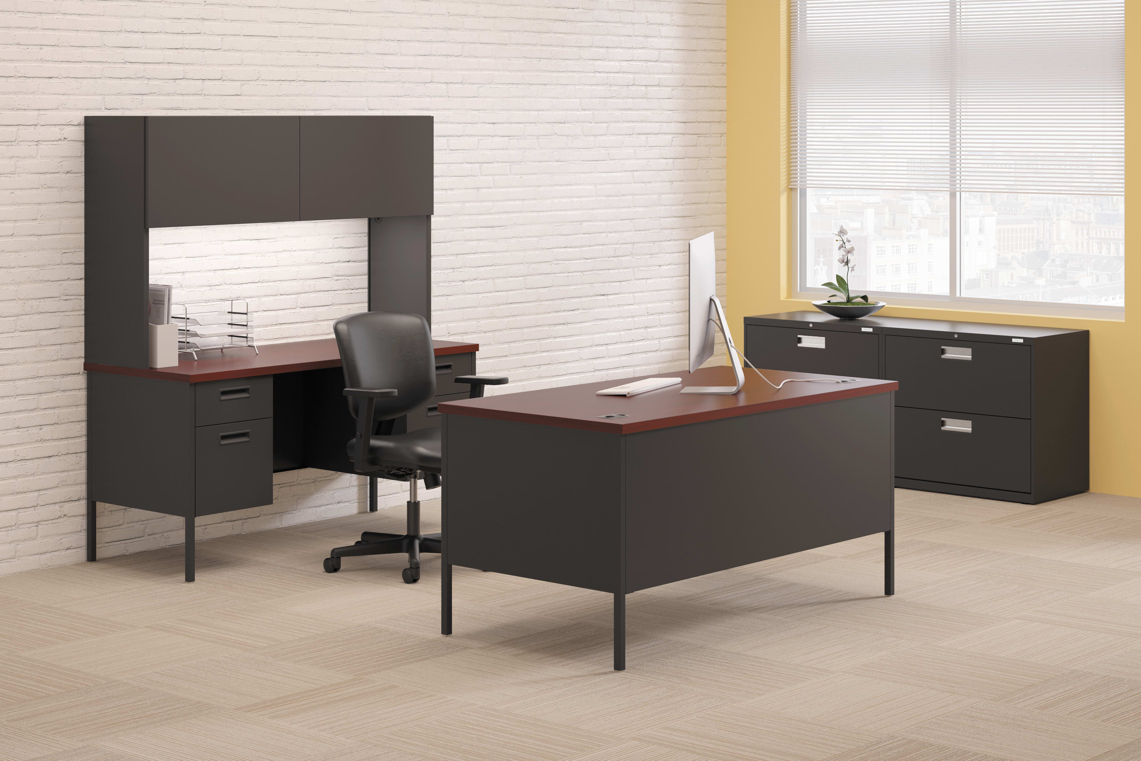 A modern and minimalist office setup with a black desk, a computer monitor, and a filing cabinet against a white brick wall background.