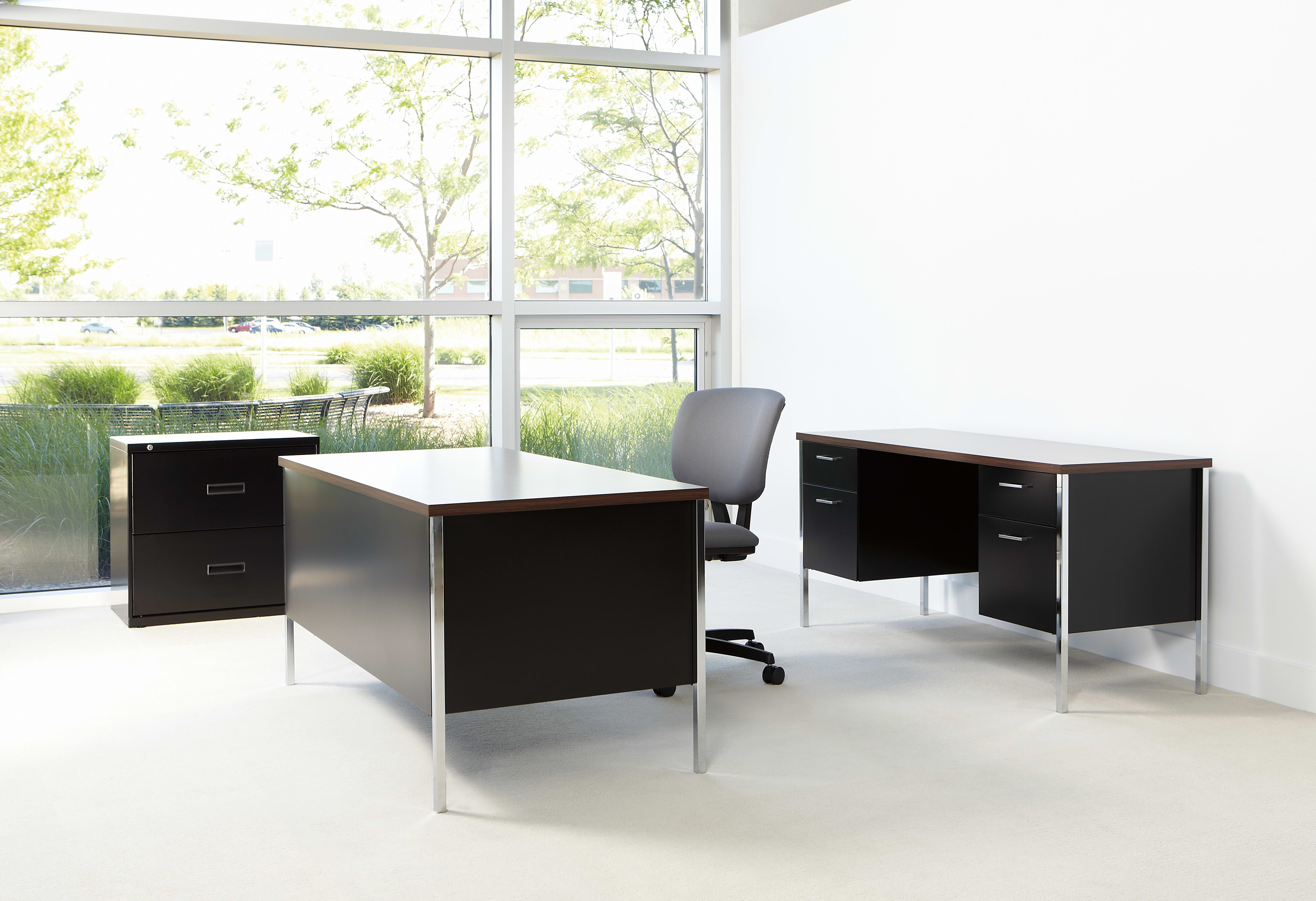 A modern and minimalist office space with a large window overlooking a lush, green outdoor environment. The room features sleek, black desks and filing cabinets, creating a clean and organized workspace.
