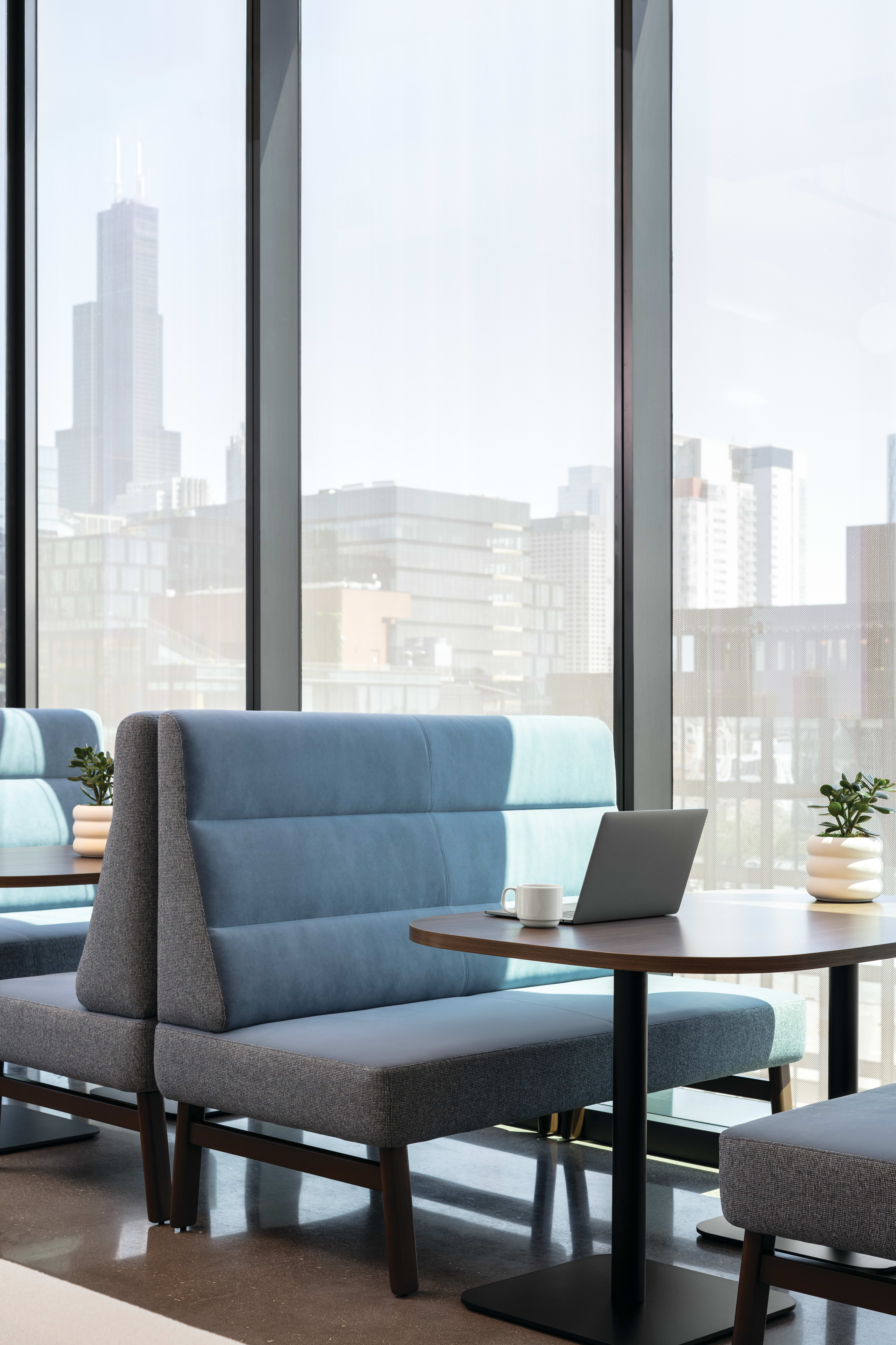 Round pedestal table with wood top and black base, paired with soft seating for casual work or conversation.