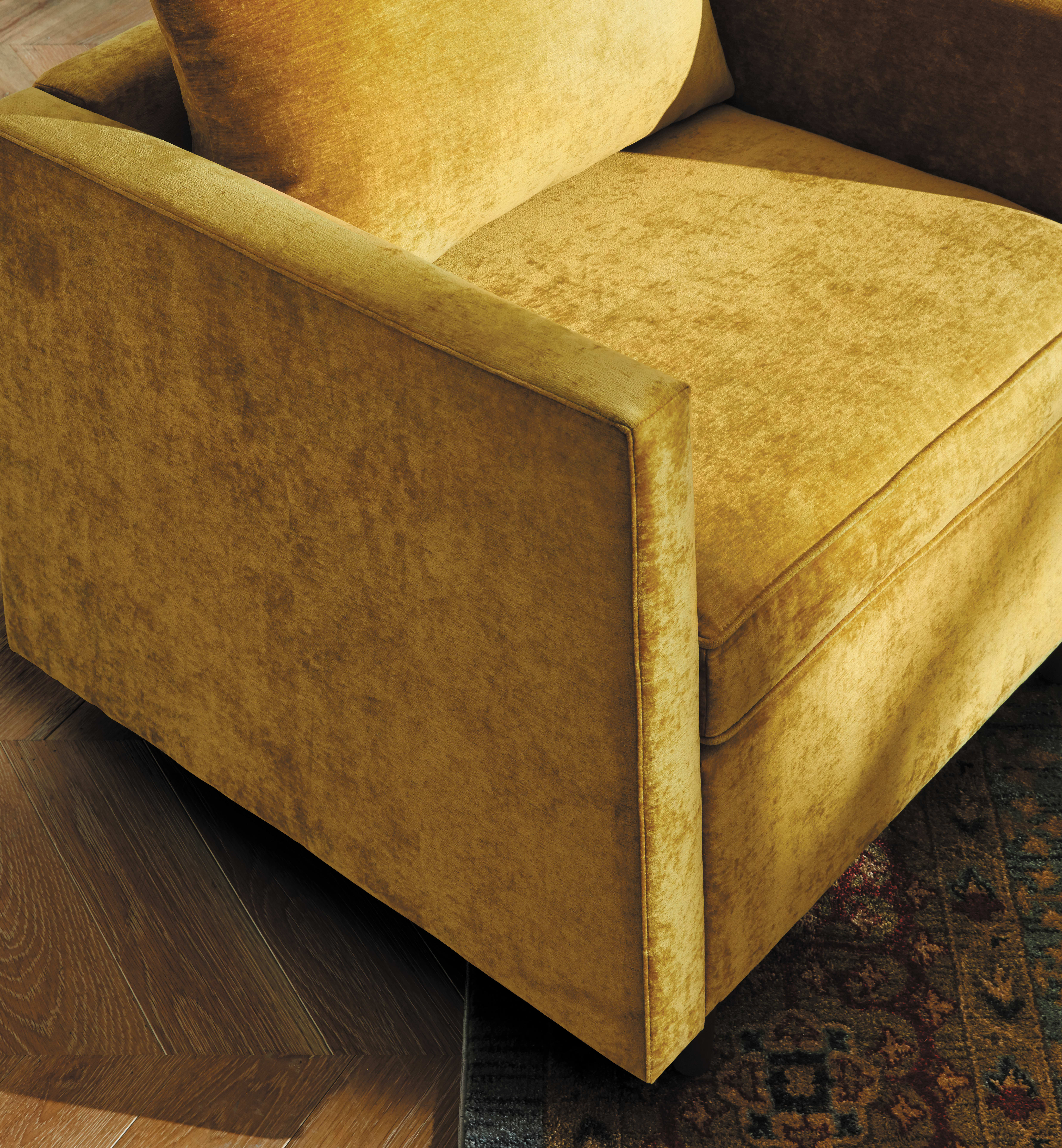 A plush, mustard-colored sofa sits on a patterned rug, with the wooden floor visible in the background.