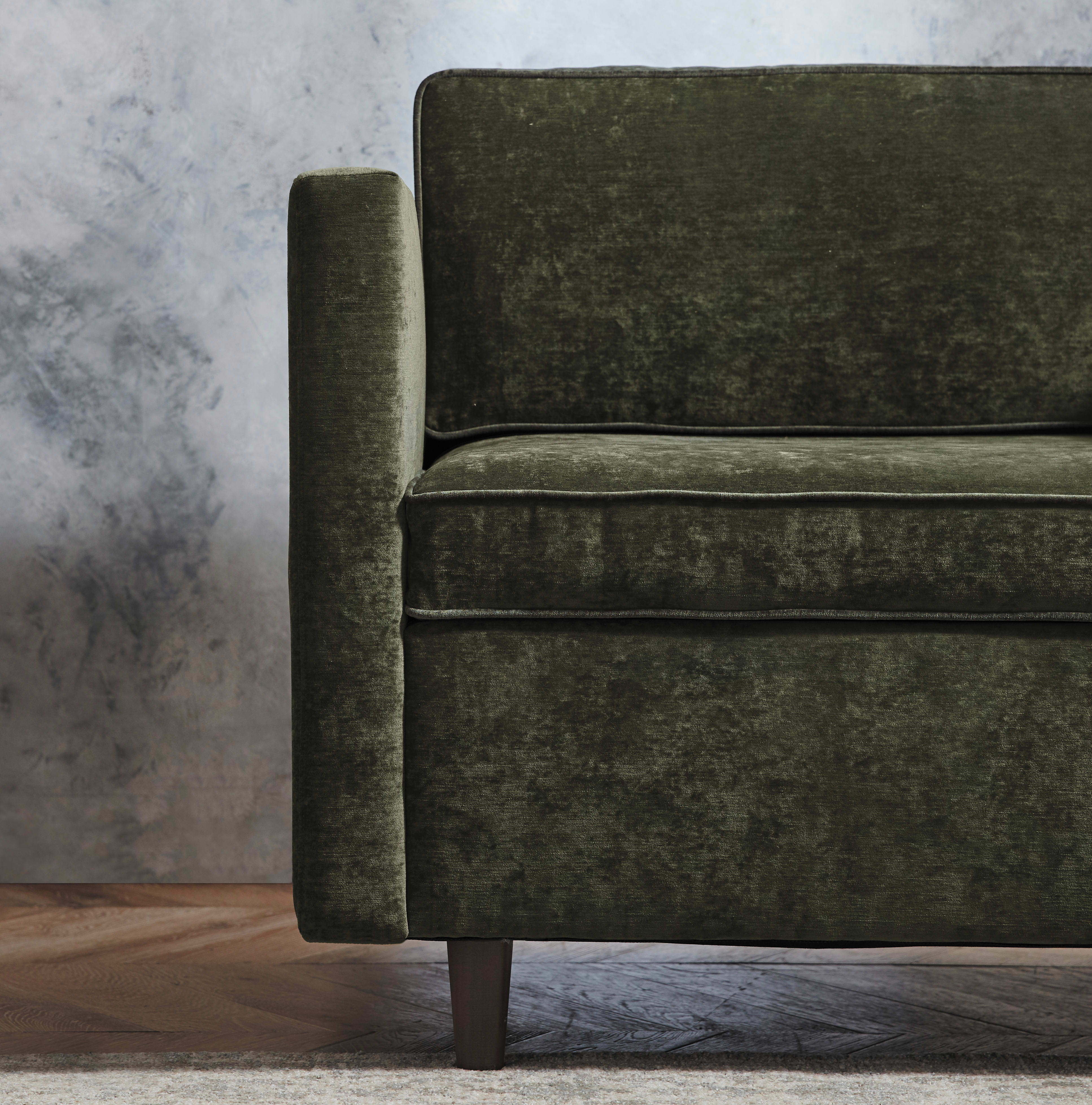 A dark green velvet sofa sits on a wooden floor against a gray background, creating a cozy and inviting atmosphere.