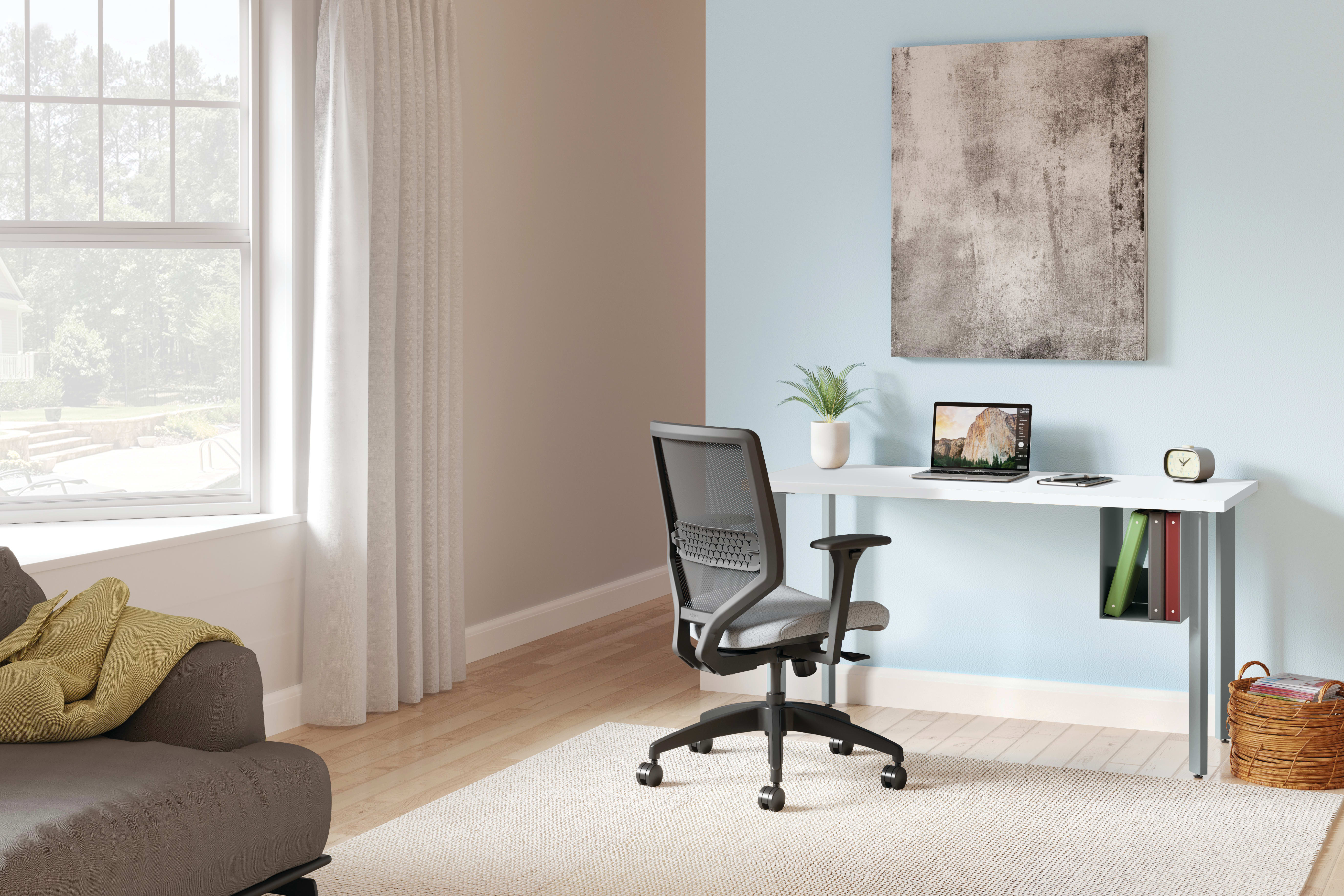 A cozy home office setup with a comfortable chair, a desk with a laptop and decor, and a large window providing natural light in a neutral-toned living space.