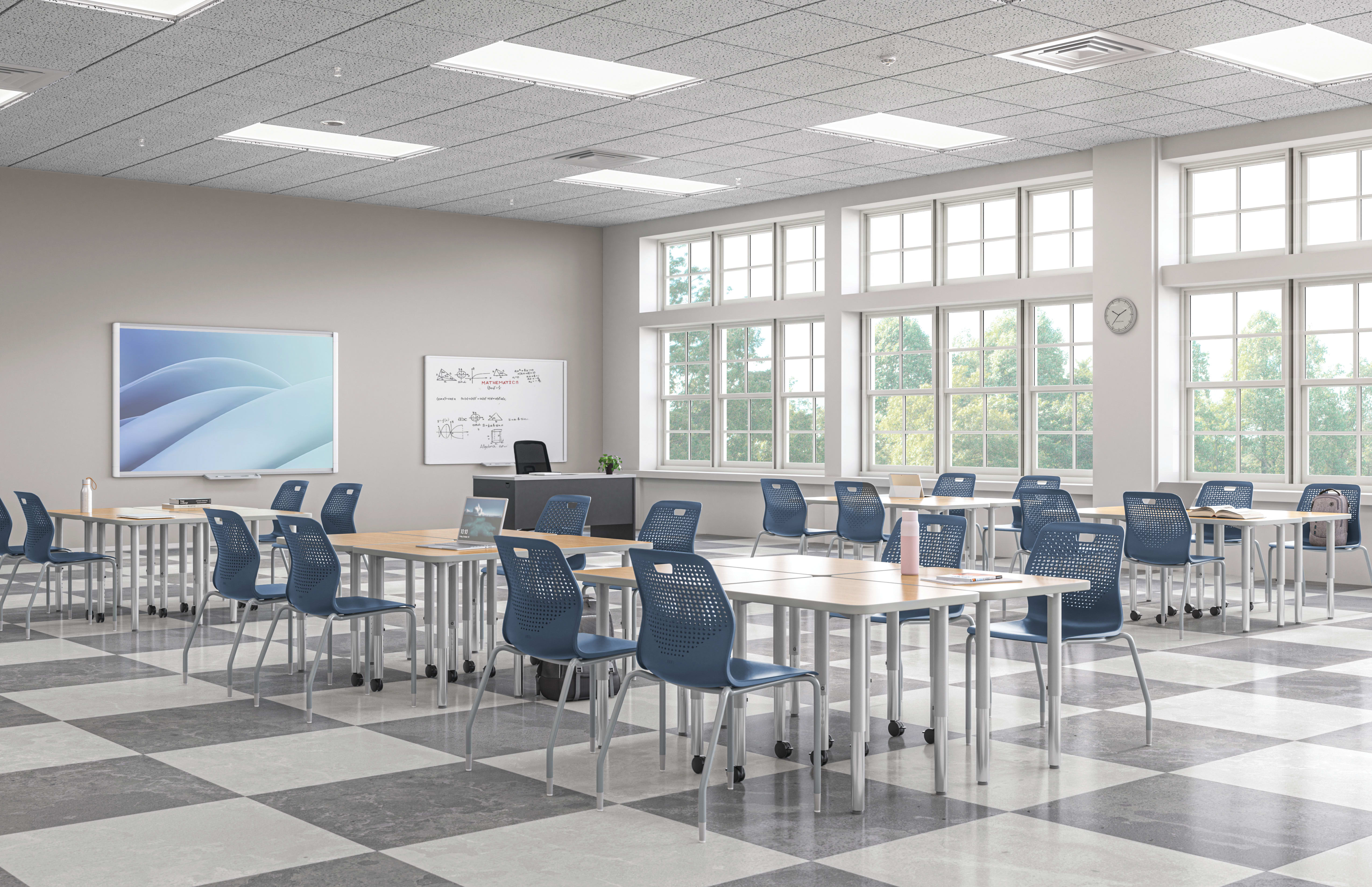 Bright modern classroom with movable tables, blue chairs, whiteboard displays, and large windows bringing in natural light.