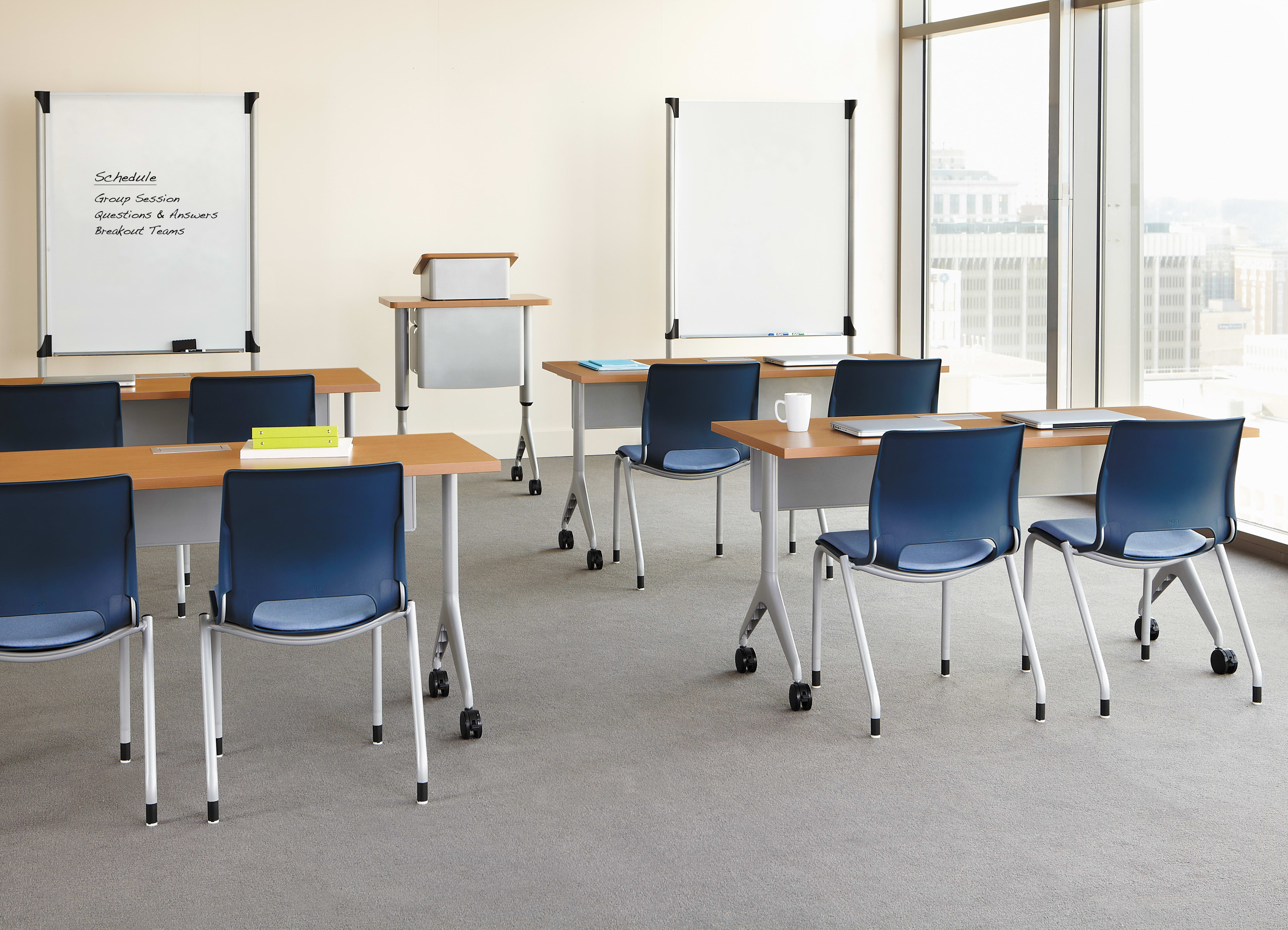 An empty classroom with desks, chairs, and whiteboards, with a large window overlooking a cityscape in the background.