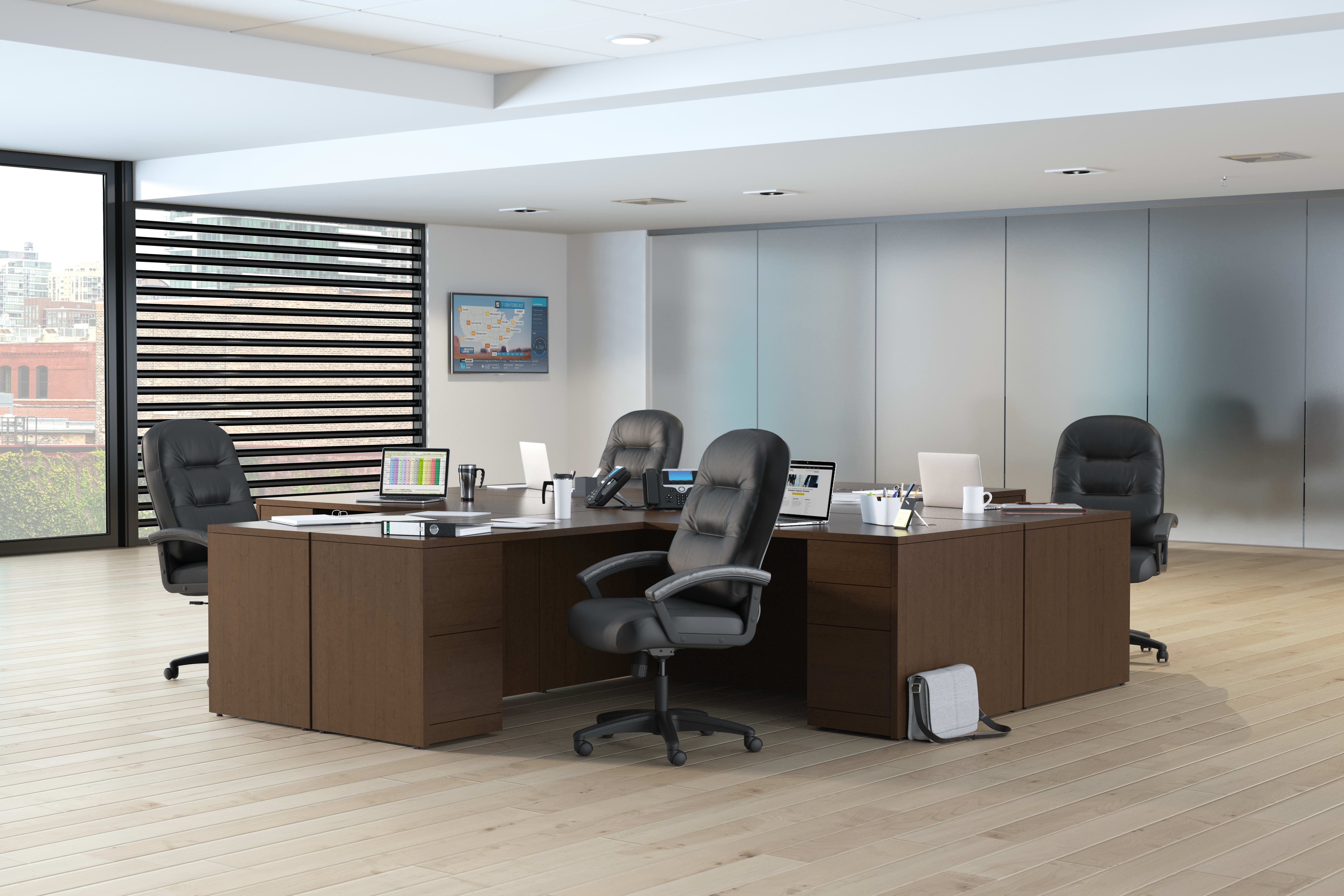 A modern and minimalist office space with wooden desks, black office chairs, and a striped partition wall in the background.