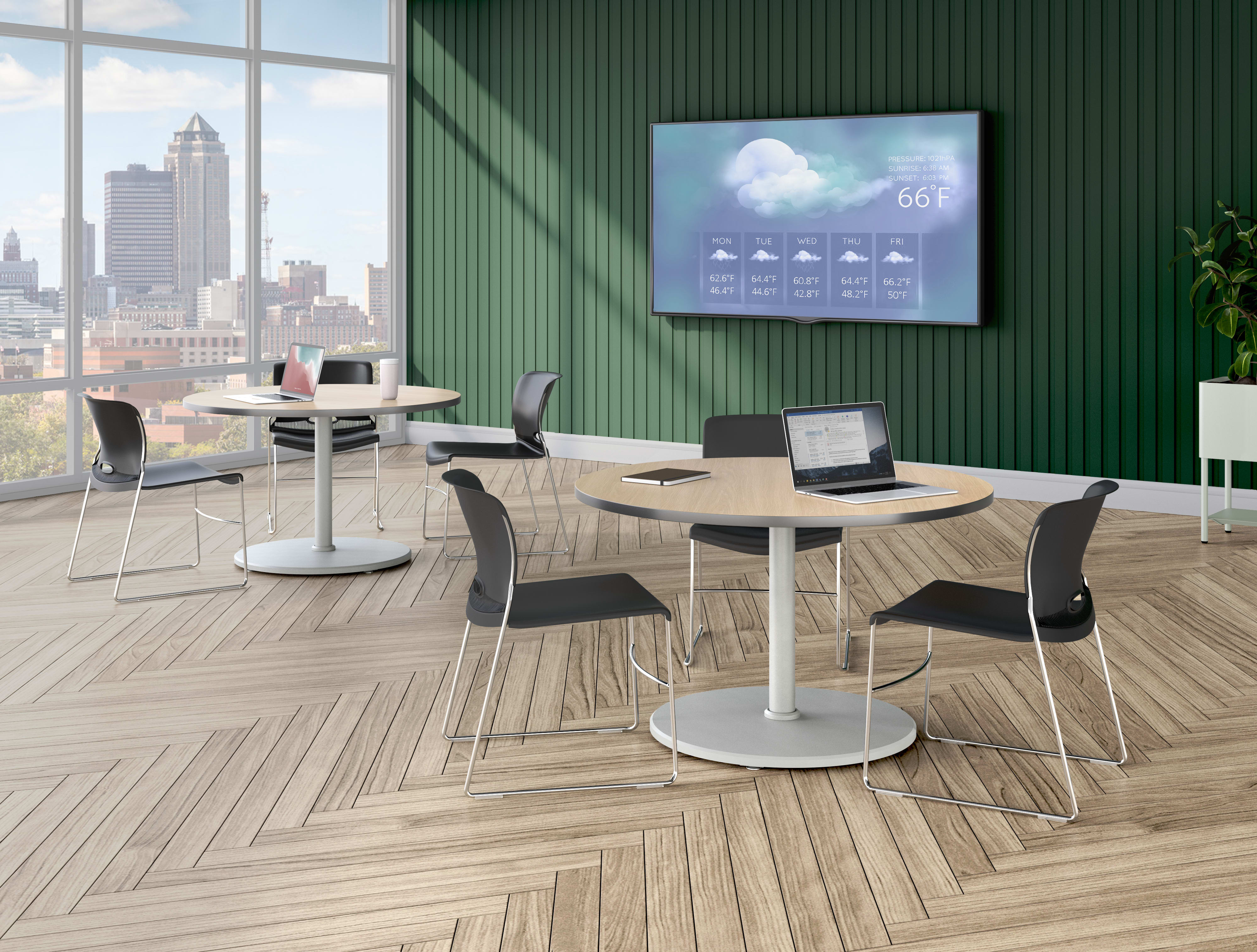 A modern lounge area with round tables, black chairs, a large wall-mounted display showing weather information, and floor-to-ceiling windows overlooking a city skyline.