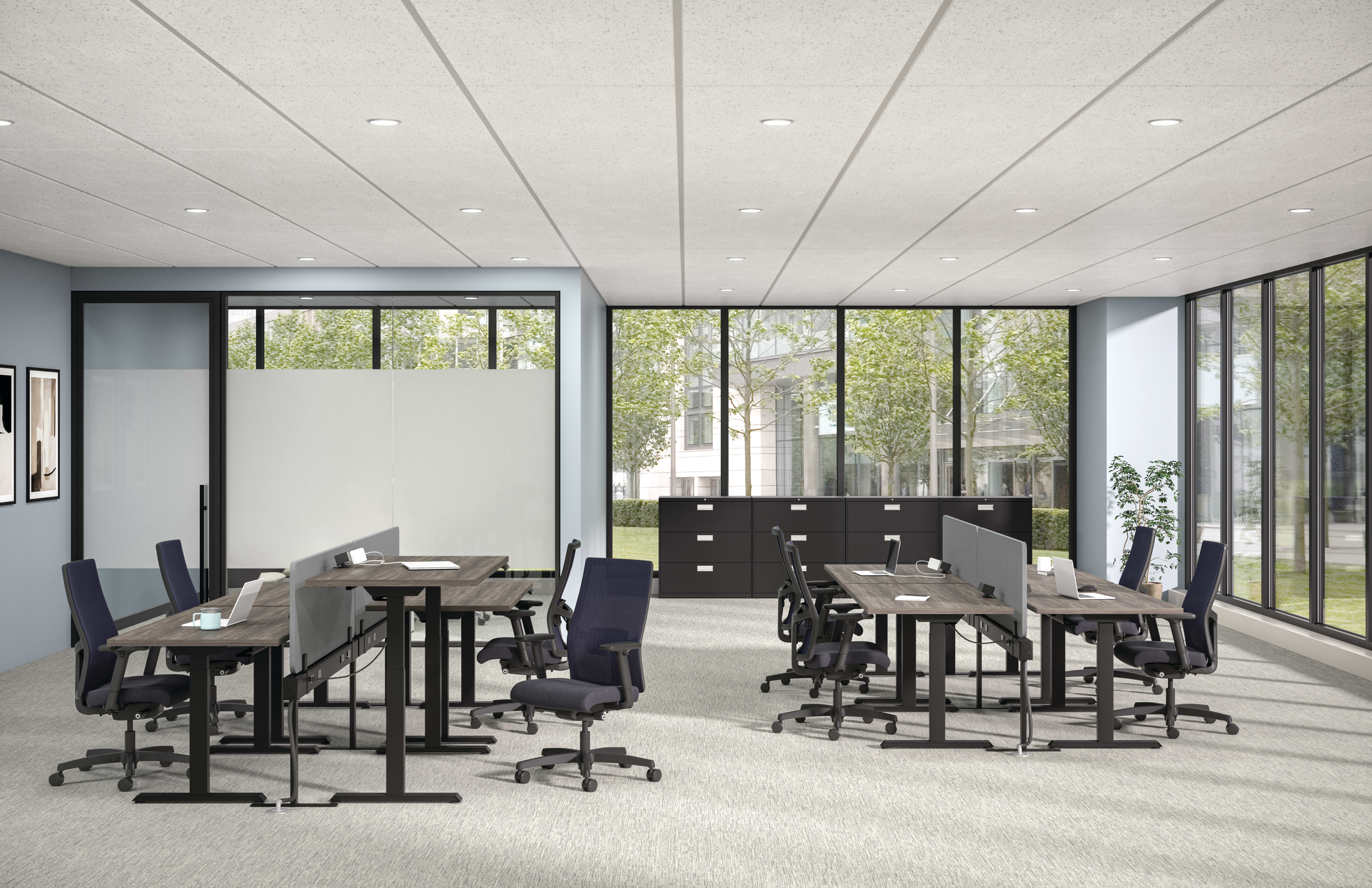 Modern open office with benching desks, task chairs, privacy panels, storage cabinets, and large windows with greenery view.