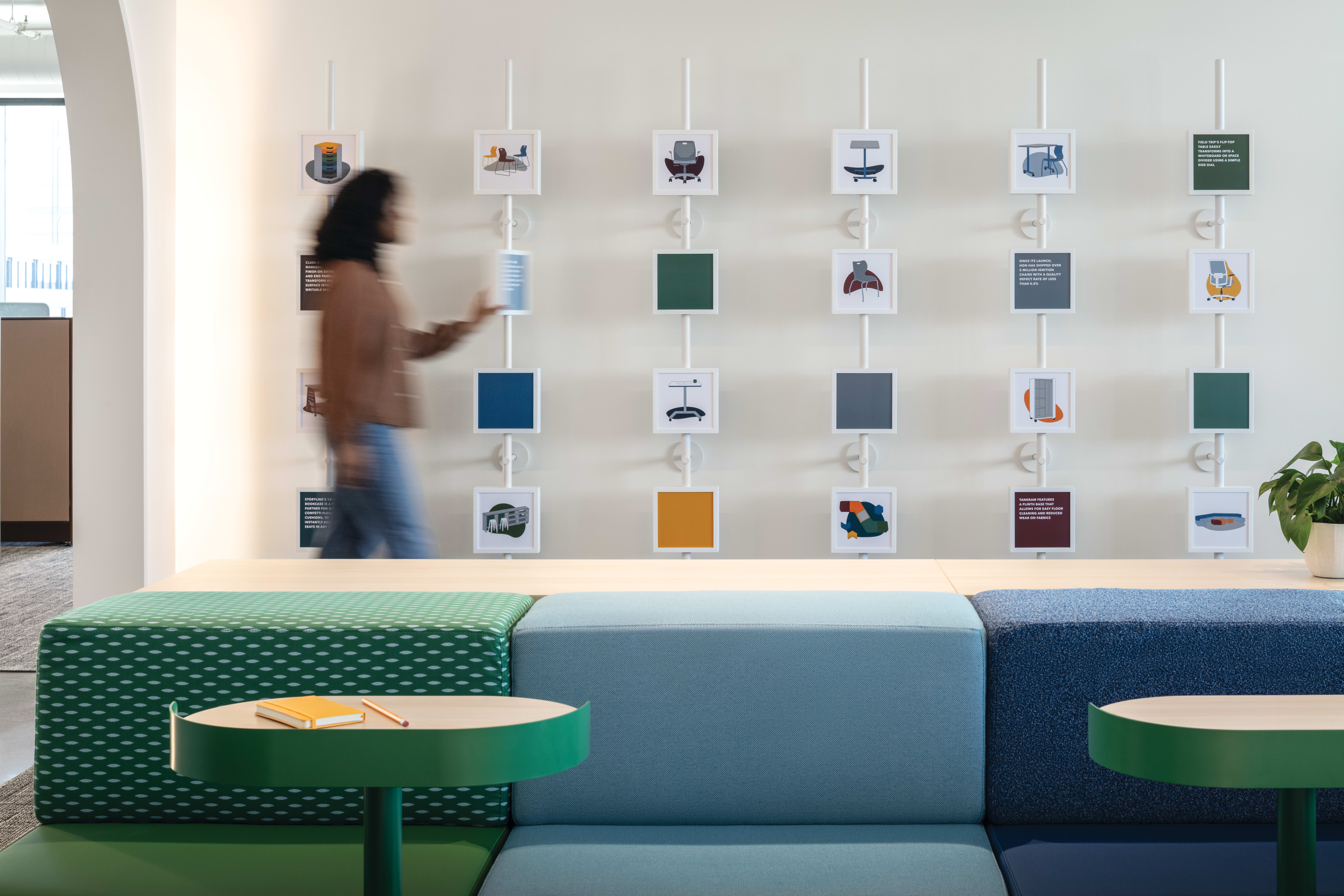 Modular upholstered bench seating with patterned and textured fabrics, round café tables in contrasting finishes, and coordinated display wall system with framed product visuals.