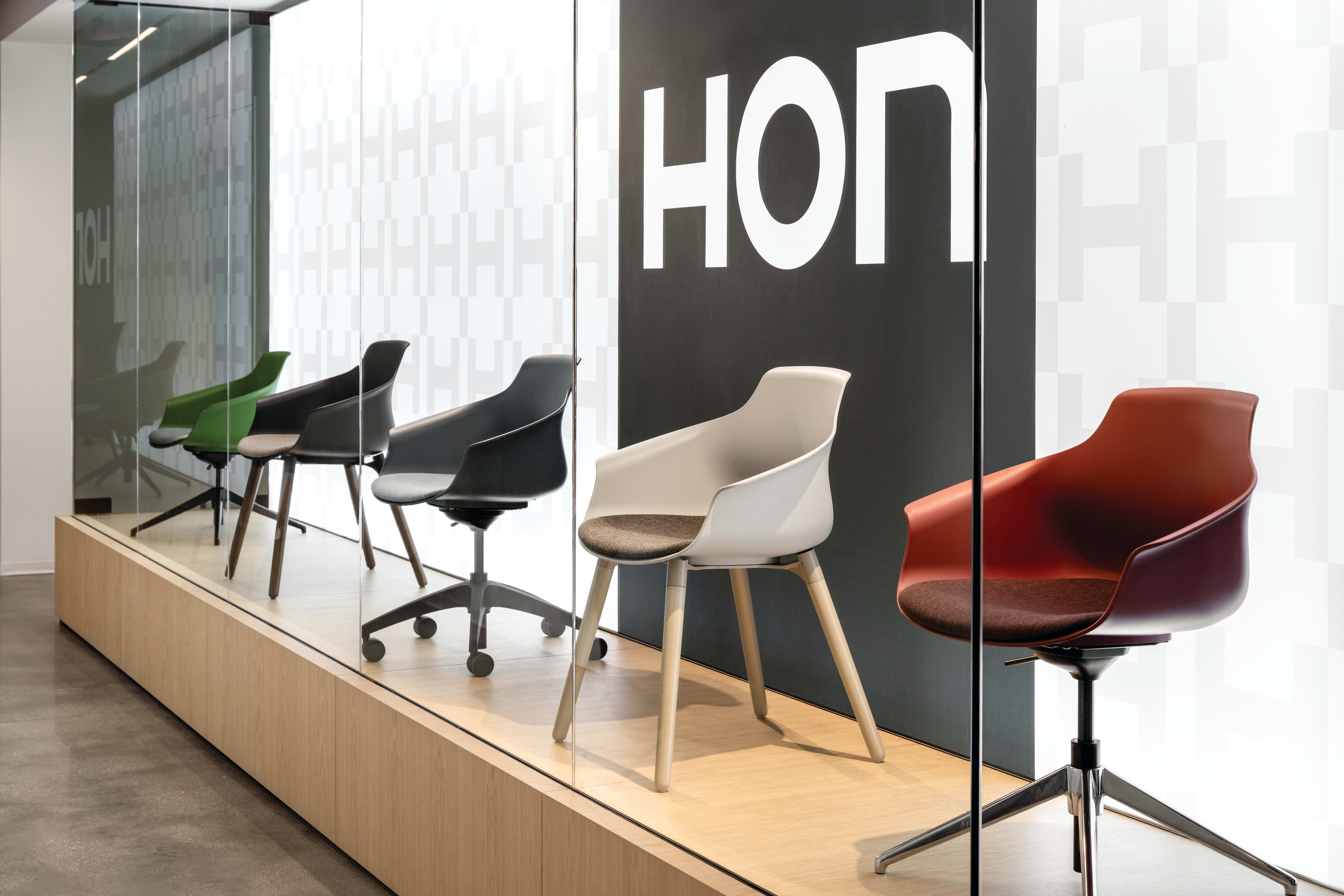 Display platform featuring a curated range of molded shell chairs with upholstered seats, presented on a raised wood base with mixed leg styles including wood, swivel, and four-star bases.