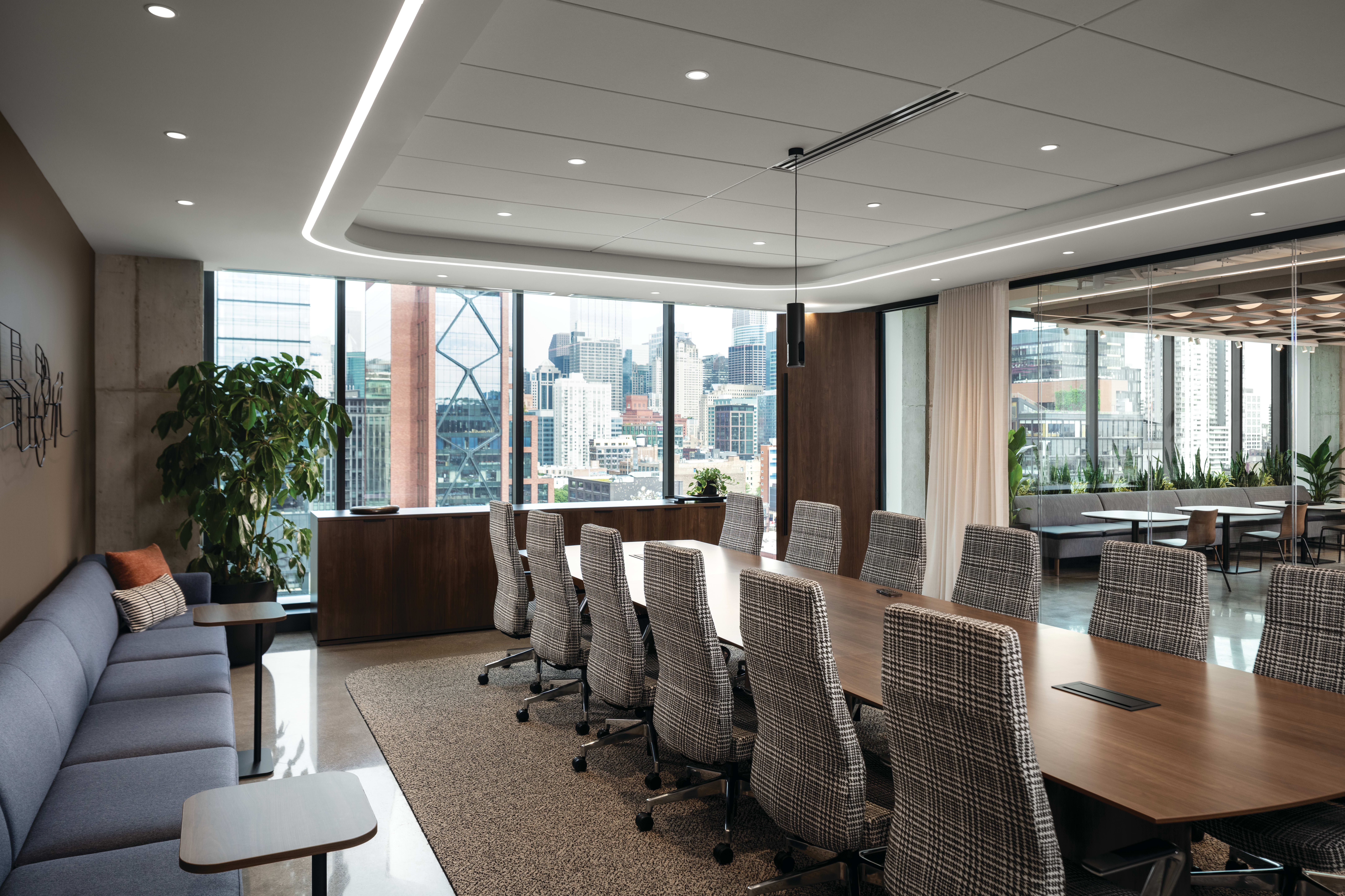 Conference seating area with upholstered rolling chairs, lounge sofa with cushioned seating, and compact side tables with wood tops and slim bases.