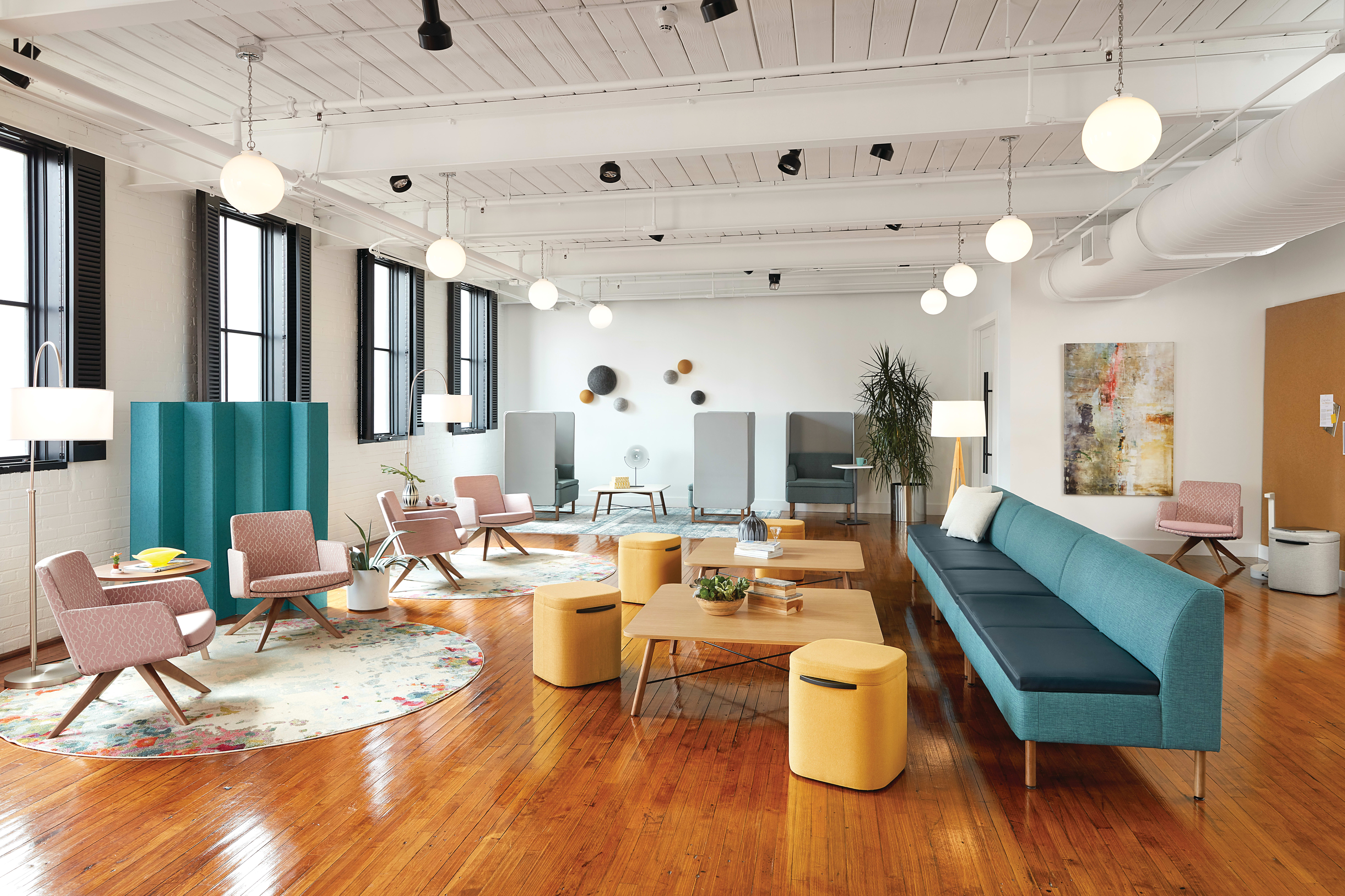 A modern and vibrant office space with a mix of comfortable seating, colorful accents, and natural lighting from the large windows.