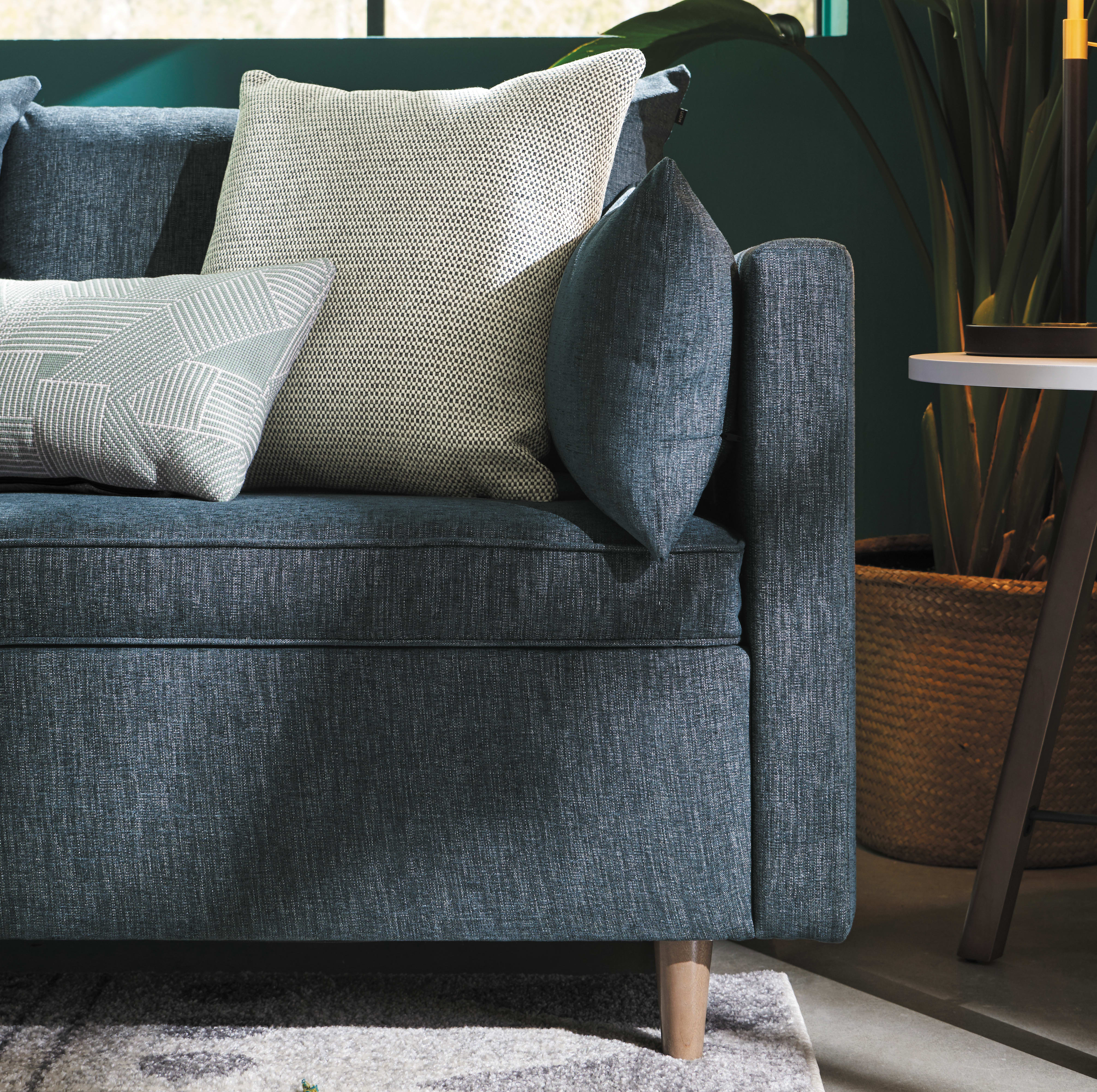A cozy gray sofa with plush pillows sits in a warm, inviting living space, surrounded by natural elements like potted plants and a woven basket.