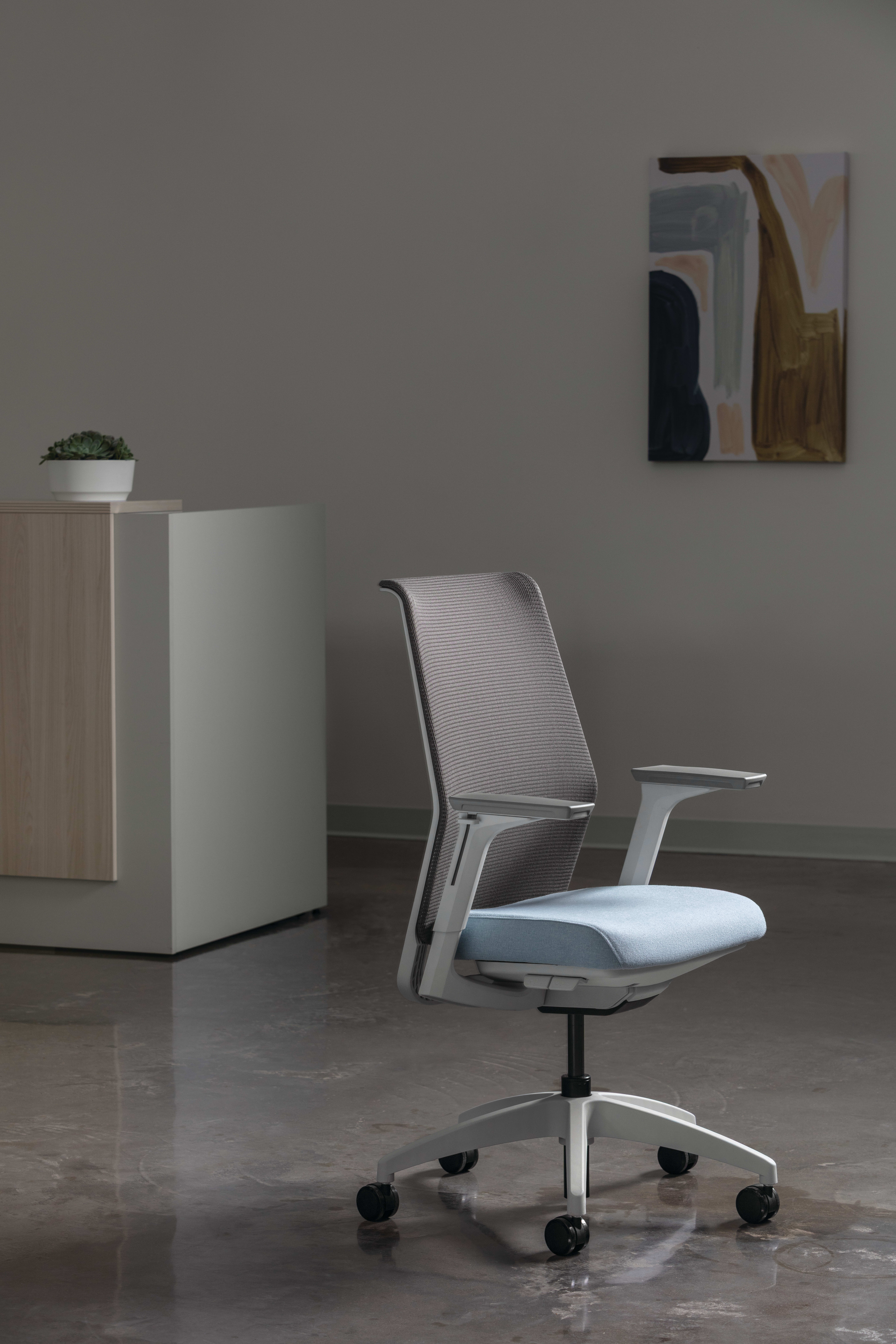 Modern task chair with a gray mesh back, light blue upholstered seat, and adjustable armrests, shown in a contemporary office setting with a neutral wall and minimalist décor.