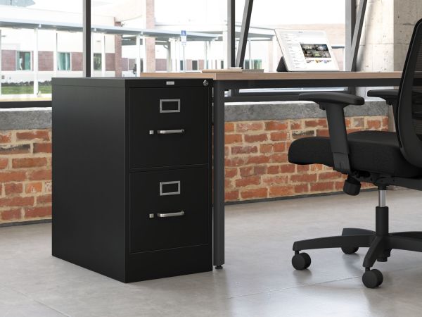 A black filing cabinet stands in the foreground, with a desk and office chair visible in the background. The room features exposed brick walls, creating a modern and industrial aesthetic.