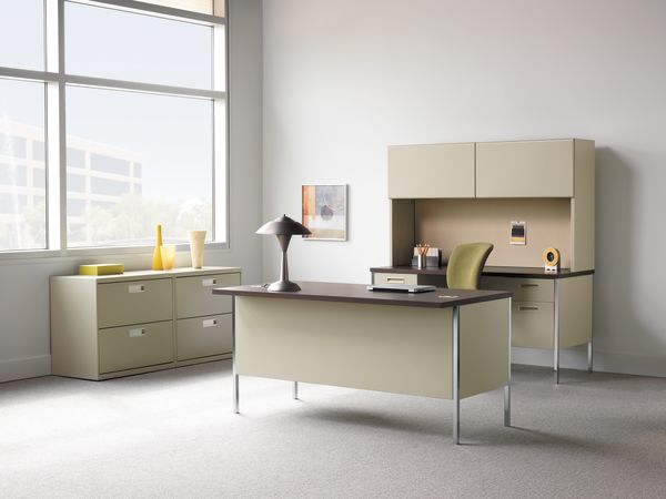 A modern, minimalist office space with a desk, storage cabinets, and a large window providing natural light.