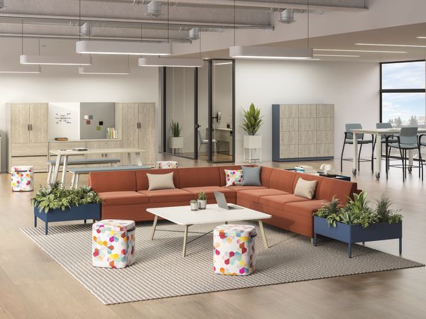 HON West Hill L-shaped sofa centered in a working-lounge with storage, lockers and standing mobile tables. 