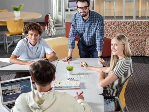 Students and a teacher collaborating in a red and yellow Multi-media Center.