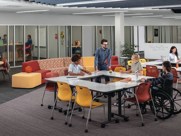 Students and teacher collaborating at Field Trip tables with red and yellow Etch chairs in a Multi-media Center with Tangram seating.
