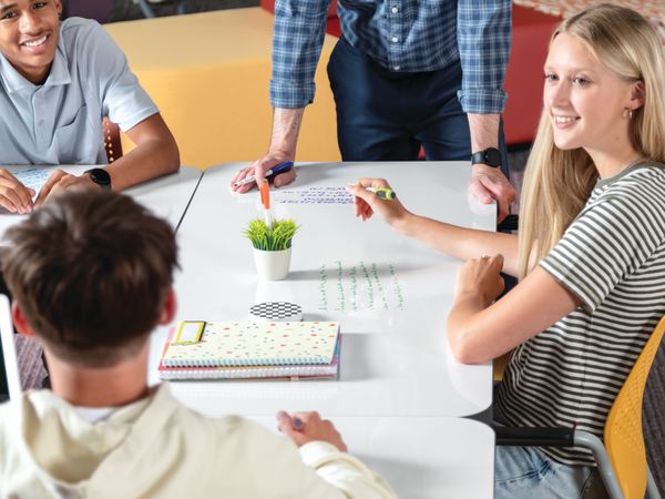 Students and teacher collaborating at Field Trip tables with red and yellow Etch chairs in a Multi-media Center with Tangram seating.