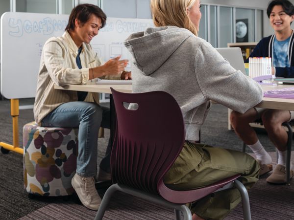 Group of students collaborating at Field Trip tables with purple SmartLink chairs in a Multi-media Center with Storyline bookcases.