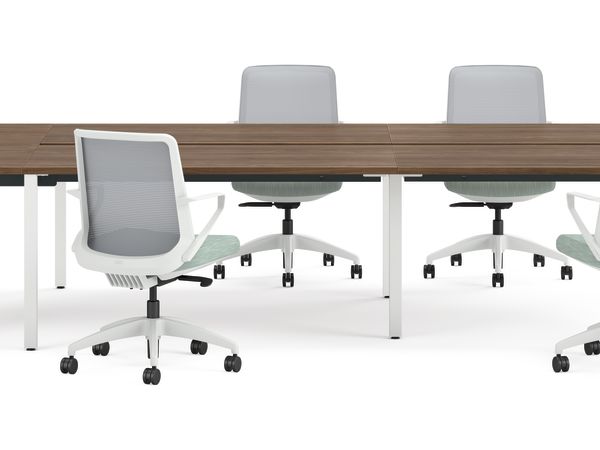 Four ergonomic office chairs around two connected rectangular desks with wooden tops and white legs, accompanied by two round upholstered stools.