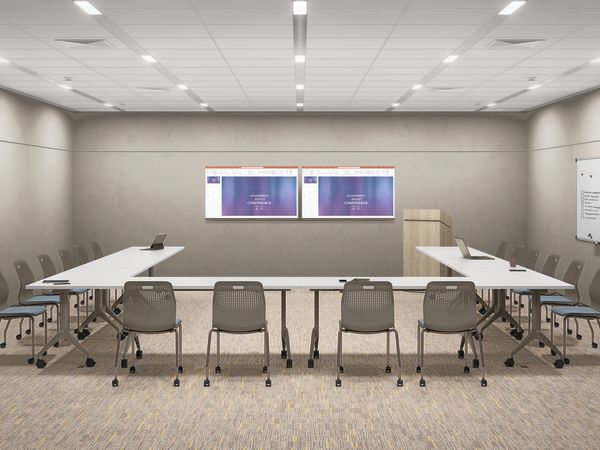 Modern training room with U-shaped tables, stackable chairs on casters, dual wall-mounted displays, lectern, whiteboard, and recessed ceiling lighting in a clean professional space.