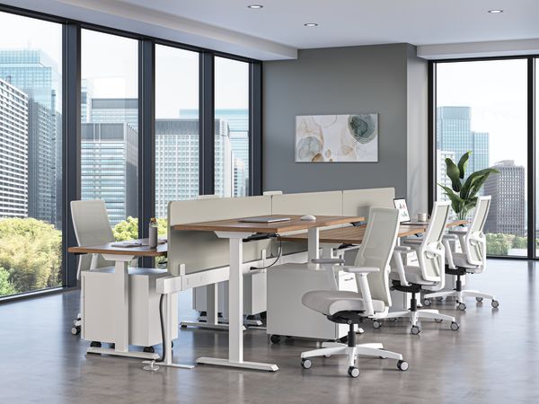 Modern office workspace with height-adjustable desks, ergonomic white chairs, and floor-to-ceiling windows overlooking a city skyline.
