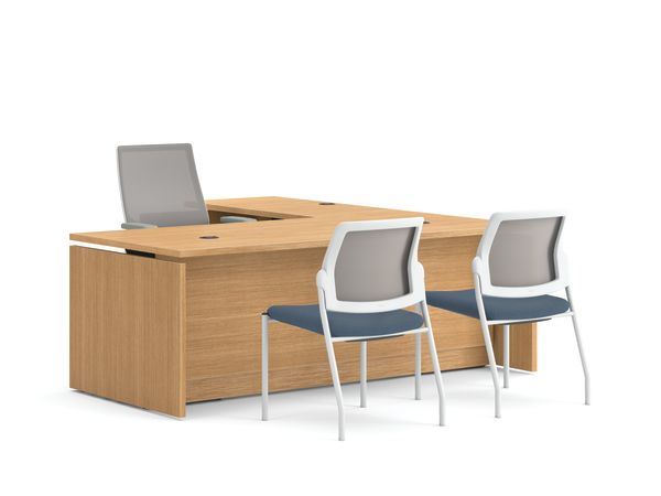 Modern wood office desk with return, mesh task chair, and two guest chairs with blue upholstered seats.