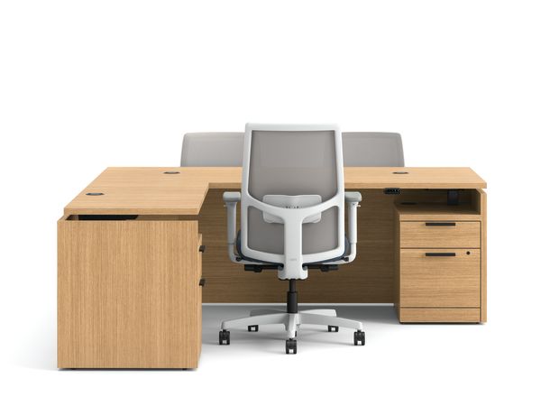 Modern wood office desk with return, mesh task chair, and two guest chairs with blue upholstered seats.