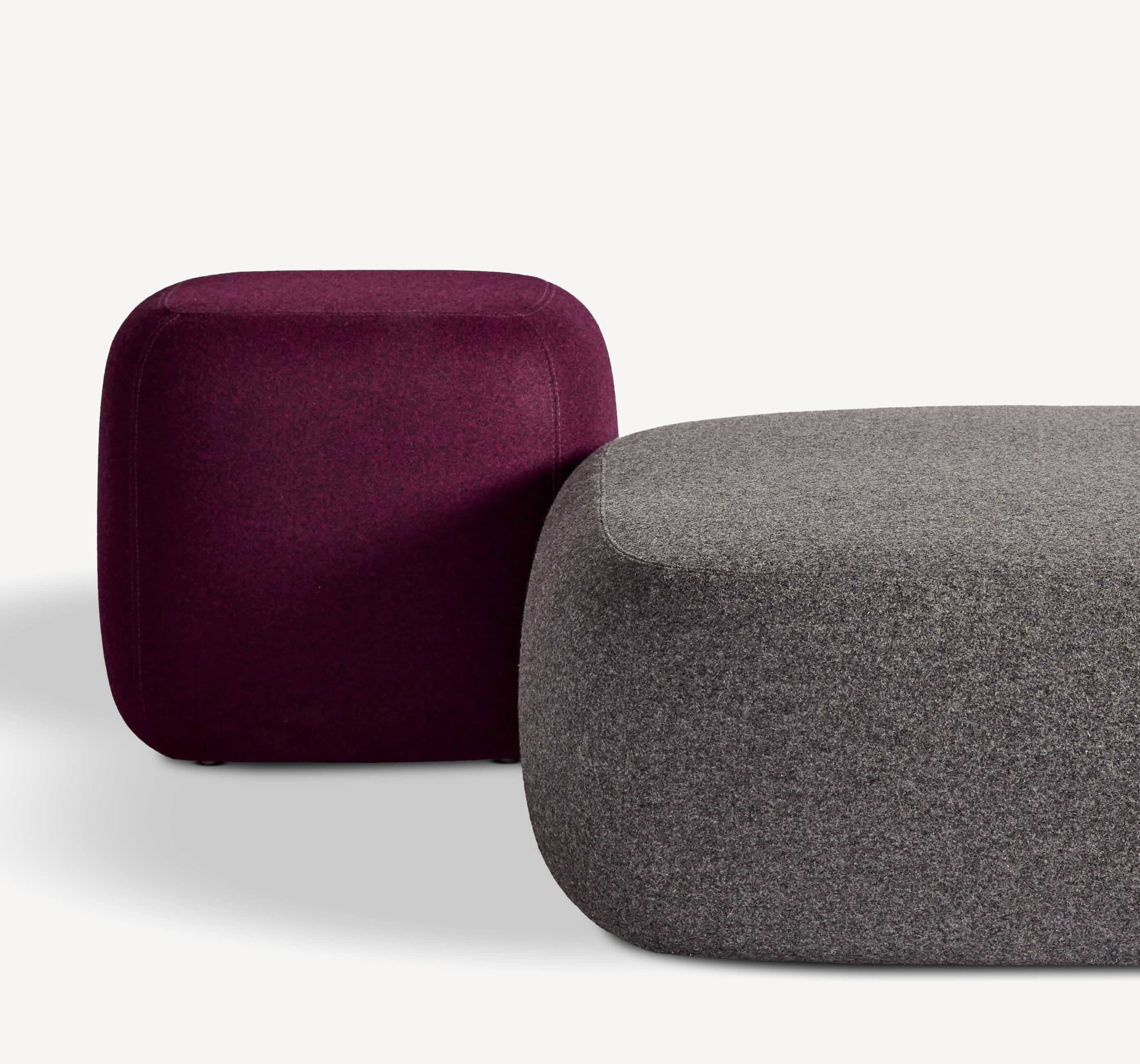 Close-up of two Corral pebble ottomans in dark grey and maroon upholstery.