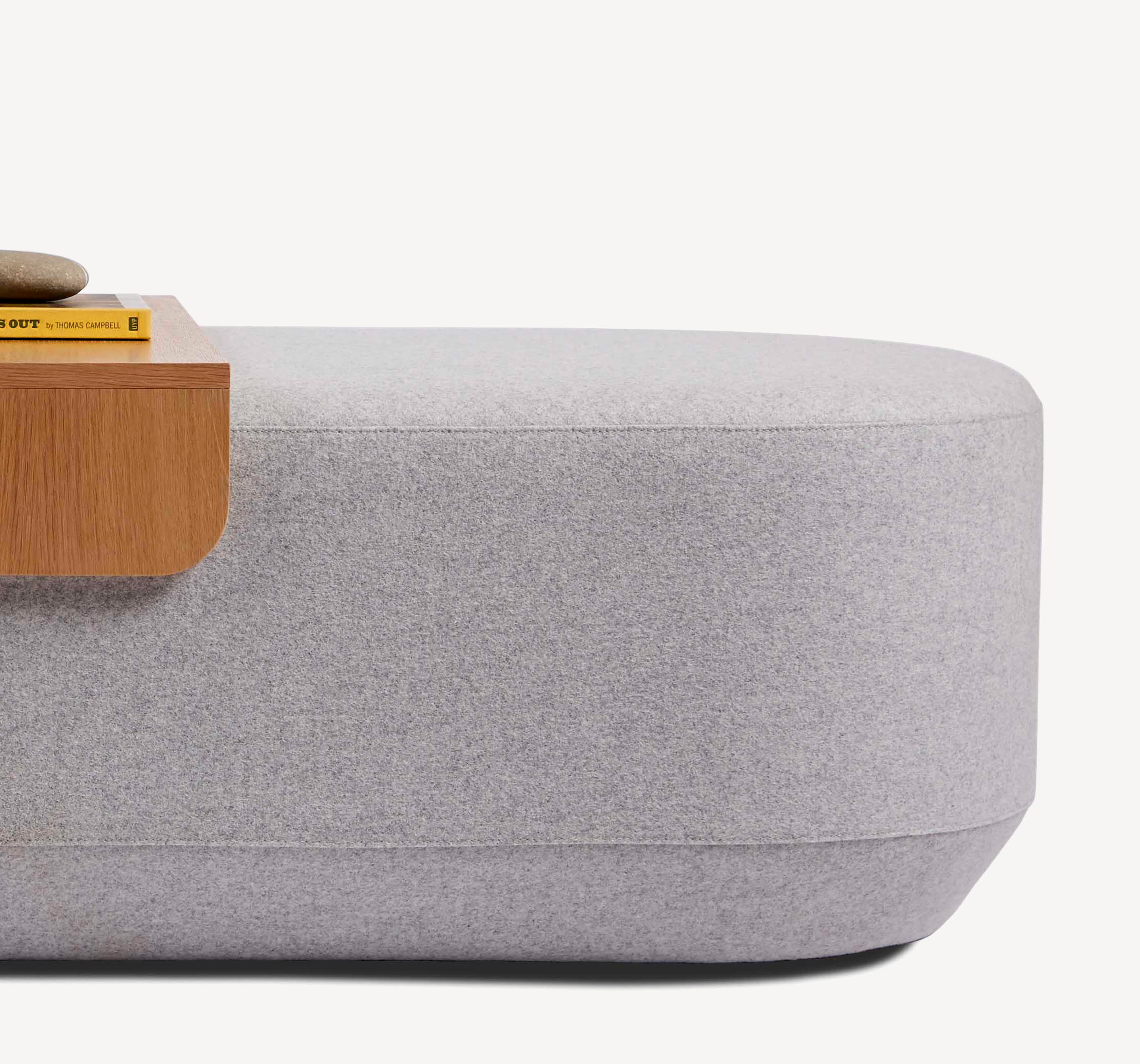 Detail view of the Corral Taper Pill ottoman in light grey upholstery with a wood moveable tray on top.