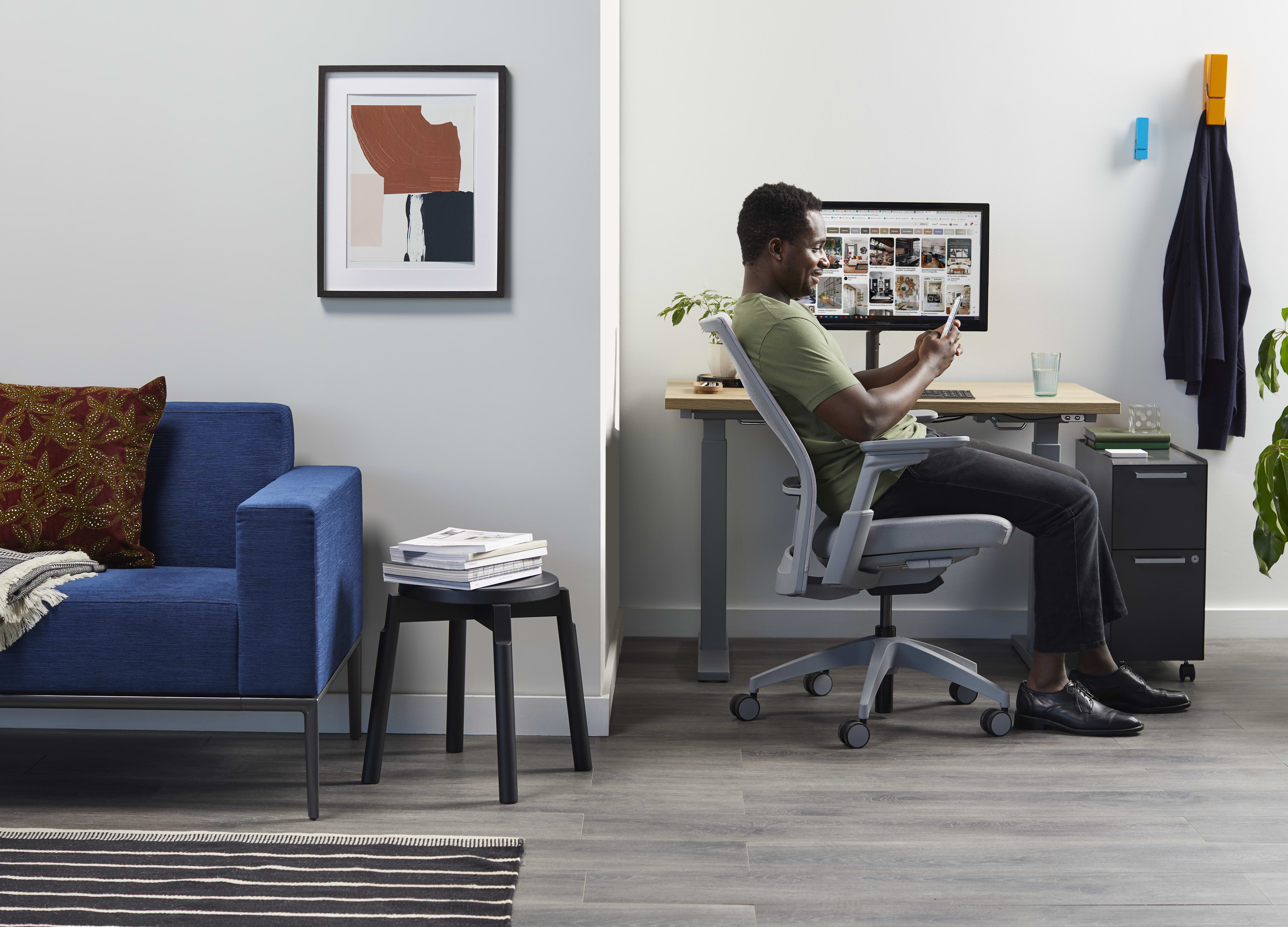 Work from home setting featuring a blue sofa, grey task chair, height-adjustable desk, and small storage.