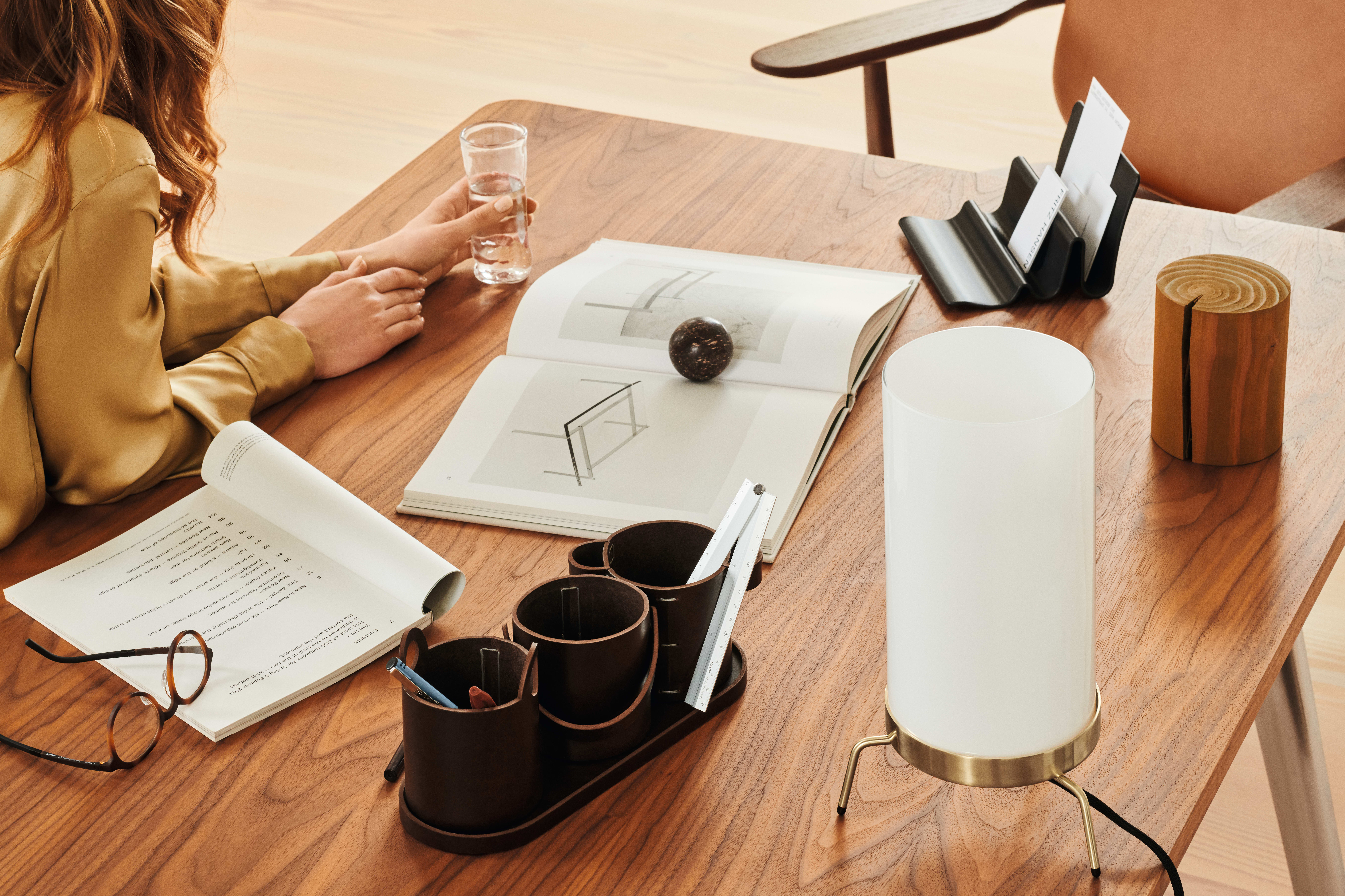 A woman sitting at a home office desk in a light wood with various books and the Buckets pen holder on top.