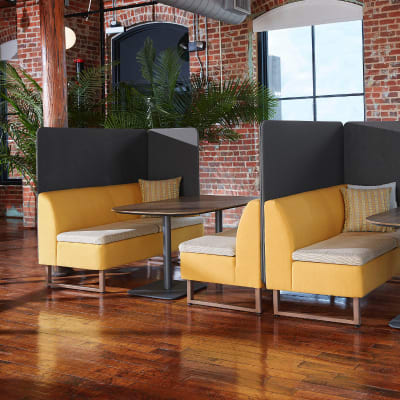 The image depicts a cozy and modern lounge area with yellow upholstered chairs, wooden tables, and large windows overlooking a scenic outdoor view.