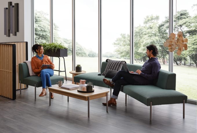 Teal, curved lounge with ounge chair in open office or lobby with light wood-toned coffee table and screen.