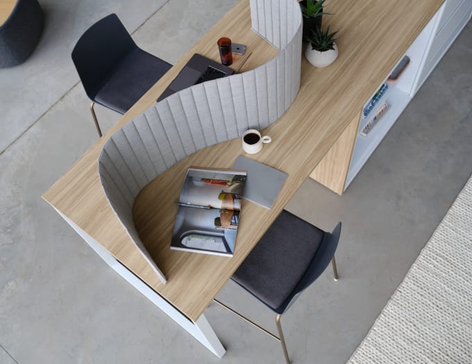 Arial view of light-wood toned counter-height table with black stool and grey acoustical screen set on top of table.