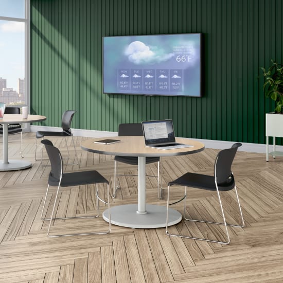 A modern lounge area with round tables, black chairs, a large wall-mounted display showing weather information, and floor-to-ceiling windows overlooking a city skyline.