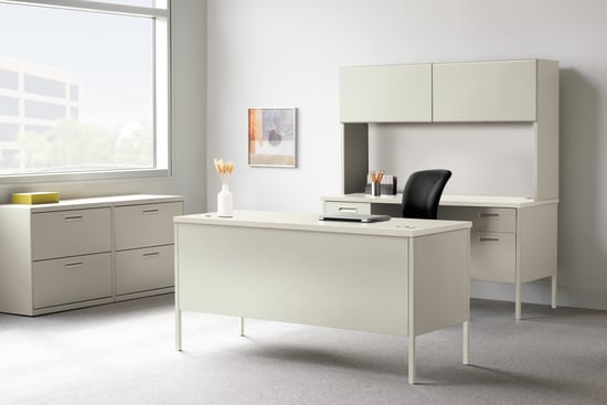A modern, minimalist office space with a white desk, cabinets, and a framed artwork on the wall, set against a bright, natural light-filled background.