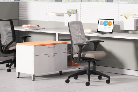 A modern, well-equipped office workspace with a desk, computer, and ergonomic office chair, set against a backdrop of large windows providing natural light.