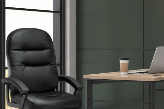 A black leather office chair sits in front of a large window, with a wooden desk and laptop visible in the background.