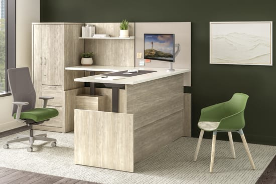 Private office with light wood desk, storage cabinet, return surface, task chair, guest chair, mounted monitor, and accent wall with window view.