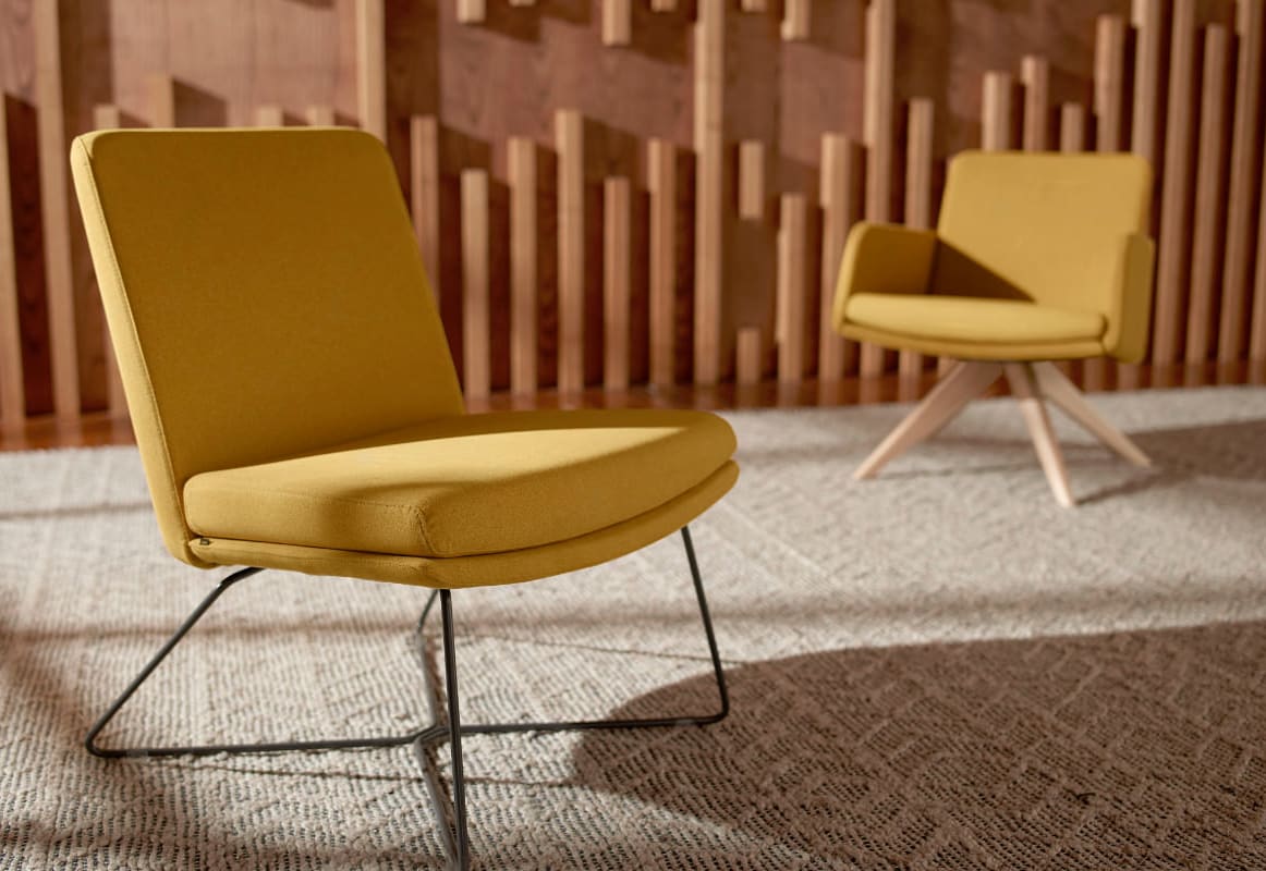 Two yellow upholstered chairs with metal frames sit on a carpeted floor in front of a wooden slatted wall.