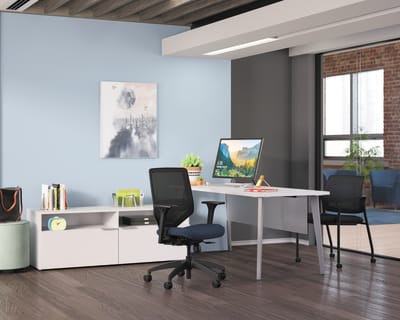 A modern, minimalist home office with a white desk, a computer monitor, and a black office chair, set against a backdrop of exposed brick walls and wooden ceiling beams.