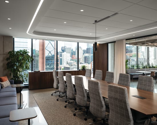 Conference seating area with upholstered rolling chairs, lounge sofa with cushioned seating, and compact side tables with wood tops and slim bases.