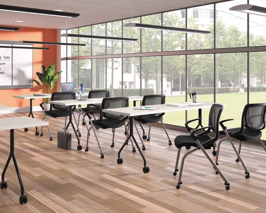 A modern, well-lit classroom with rows of desks and chairs, large windows overlooking a grassy outdoor area, and various lighting fixtures and equipment visible.
