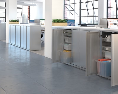 A modern and open-concept office space with a kitchen area, desks, and large windows providing ample natural light.